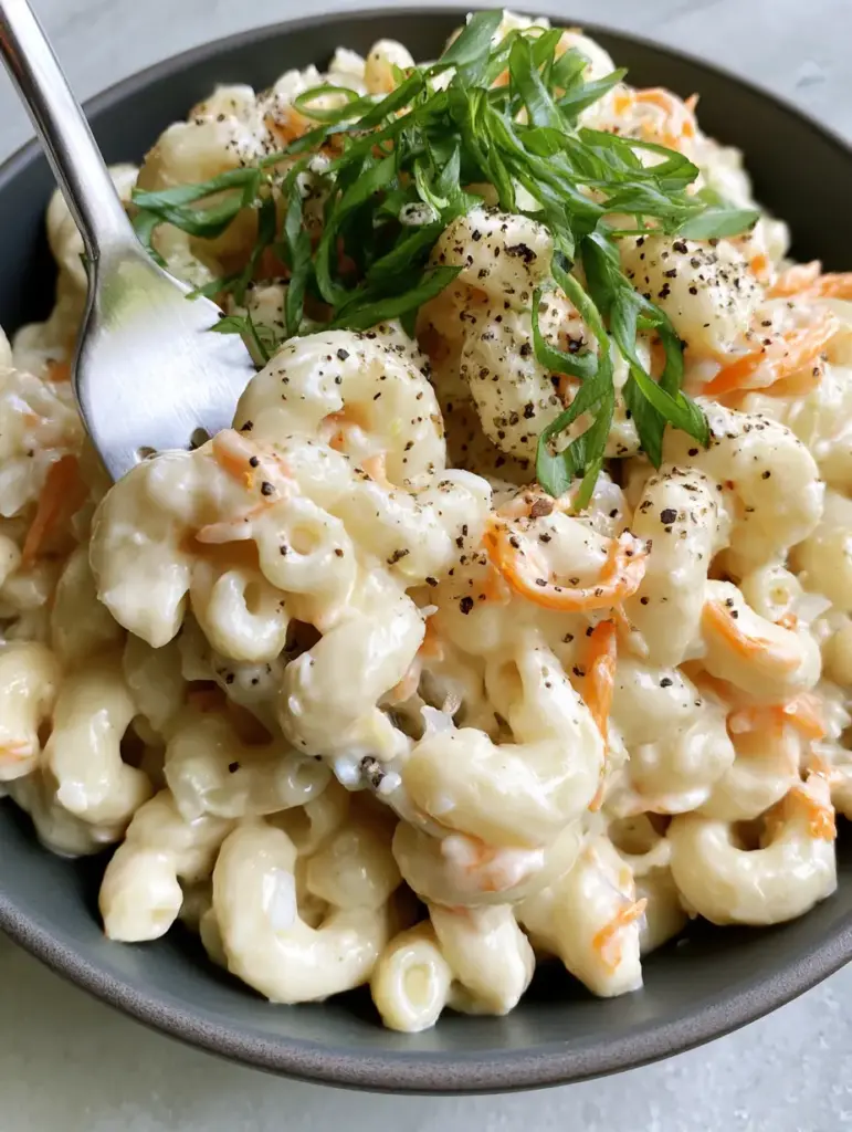 Top-down view of Hawaiian mac salad in a charcoal bowl showing fine carrot threads and cracked pepper seasoning.