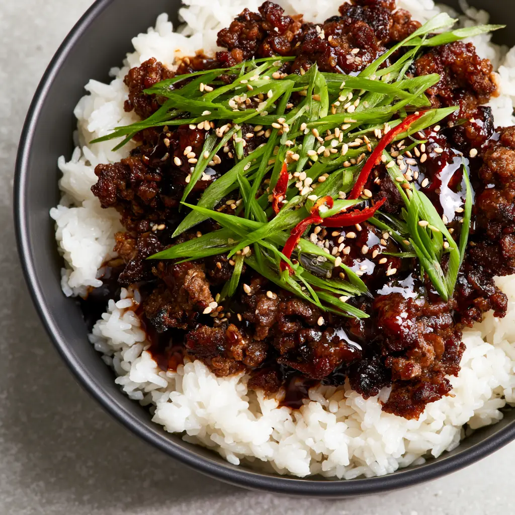 Top-down shot of a matte charcoal bowl filled with steamy jasmine rice and Korean beef bowls garnish.