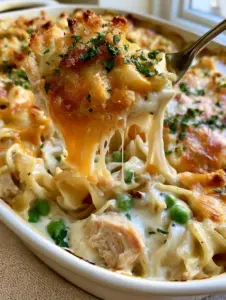 A close-up of a white ceramic dish filled with leftover turkey noodle casserole, topped with melted cheese and fresh parsley.