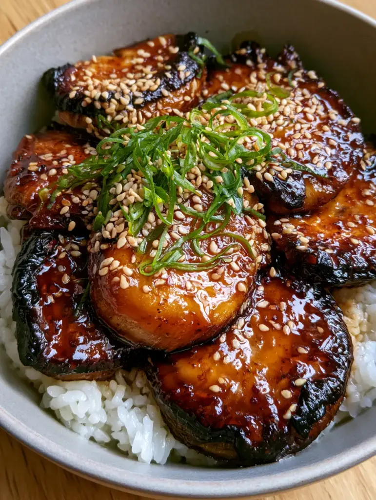 A close-up of bubbling sticky teriyaki glaze on mushrooms with sesame seed garnish.