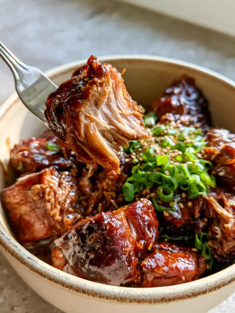 Top-down view of a cream ceramic pot filled with mahogany glazed braised pork shoulder chunks and fresh green scallions.