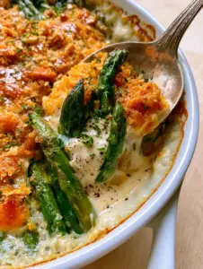 Extreme macro close-up of vibrant emerald green asparagus spears coated in velvety white cream sauce and golden Ritz crumbs.