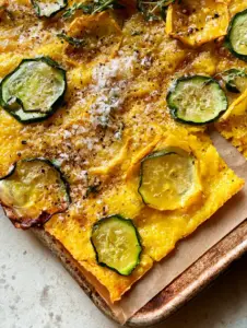 A handheld smartphone photo showing the wafer-thin profile and bubbly golden-yellow crust of a zucchini scarpaccia. (zucchini scarpaccia)