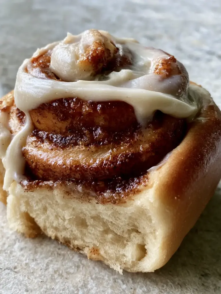 Detail of a cinnamon roll featuring a deep golden-brown exterior and dark brown sugar caramelized center. (cinnamon roll recipe)
